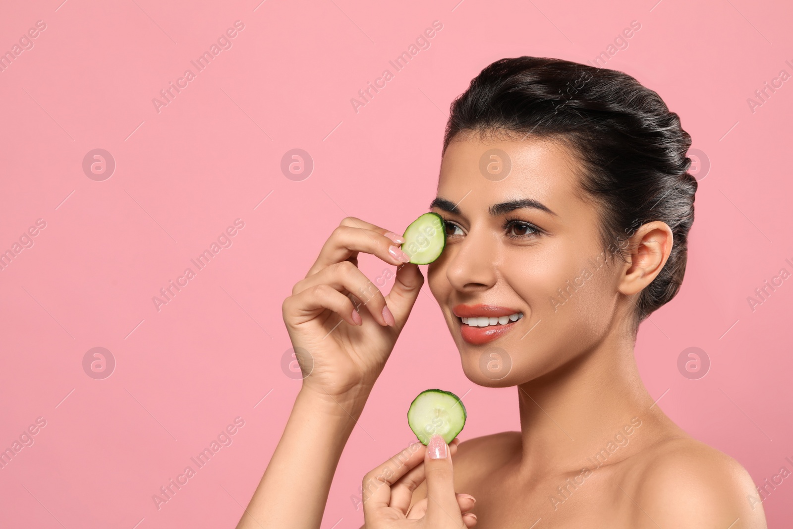 Photo of Woman covering eyes with cucumber slices on pink background, space for text. Skin care