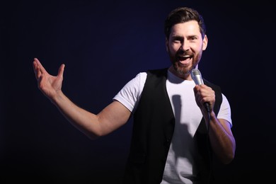 Photo of Handsome man with microphone singing on dark blue background