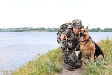 Photo of Man in military uniform with German shepherd dog near river