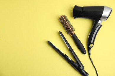 Photo of Hair dryer, straightener and brush on yellow background, flat lay. Space for text