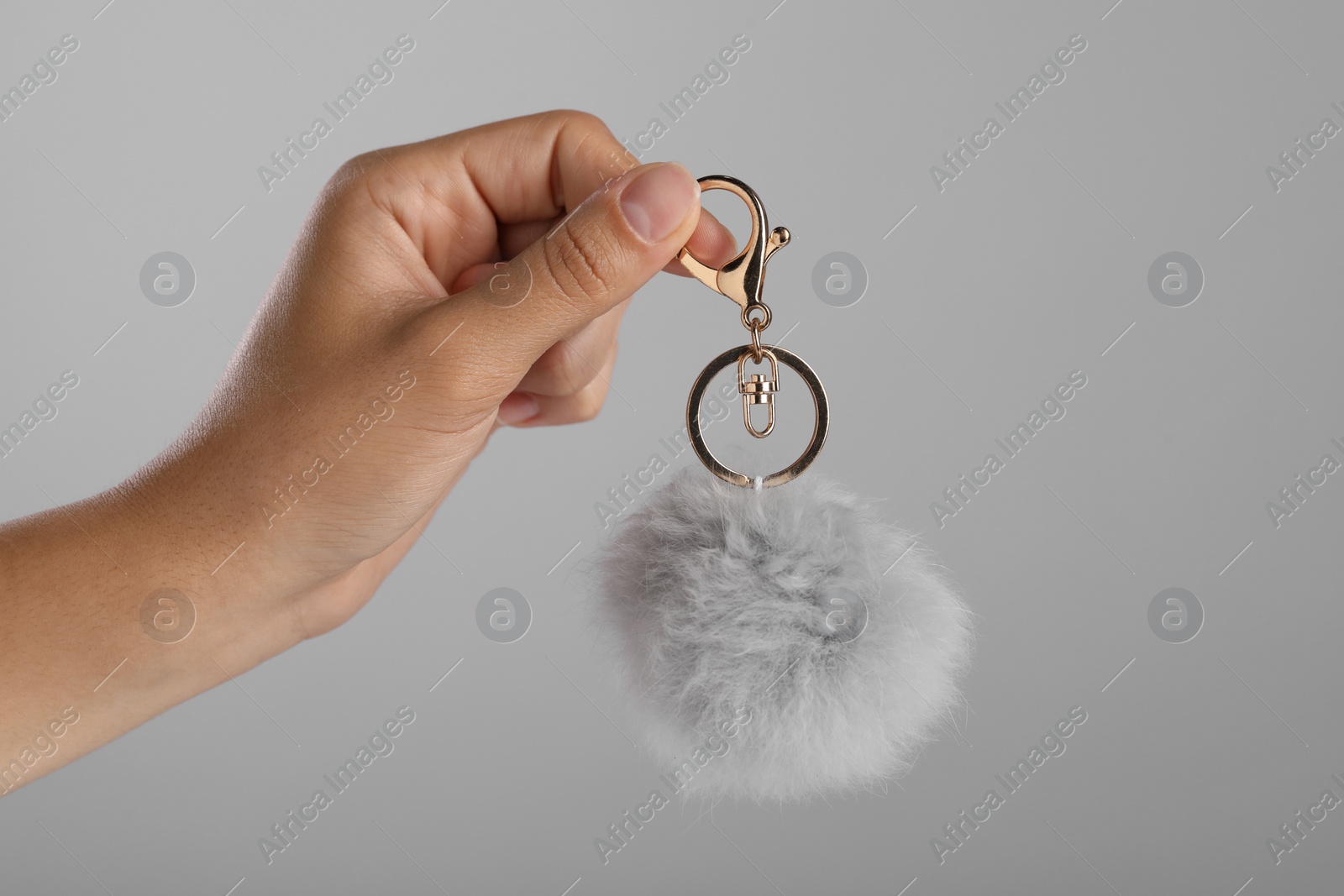 Photo of Woman holding fur keychain on grey background, closeup