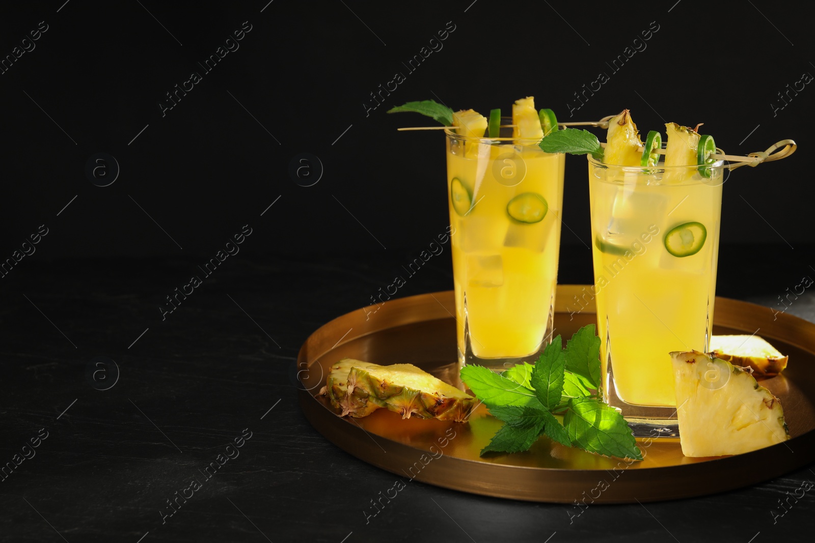 Photo of Glasses of tasty pineapple cocktail with sliced fruit, mint and chili pepper on black table. Space for text