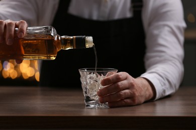 Bartender pouring whiskey from bottle into glass at bar counter indoors, closeup