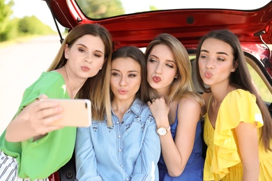 Happy beautiful young women taking selfie near car