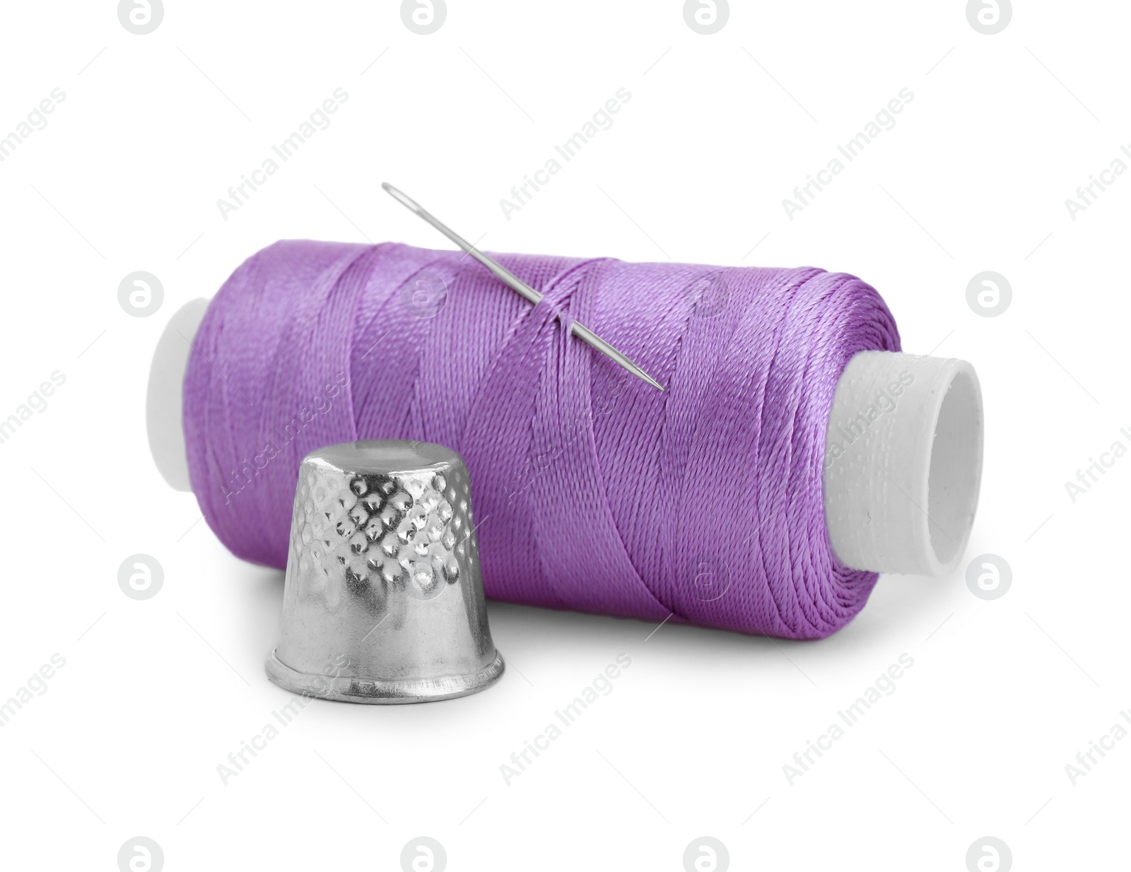 Photo of Thimble and spool of violet sewing thread with needle isolated on white