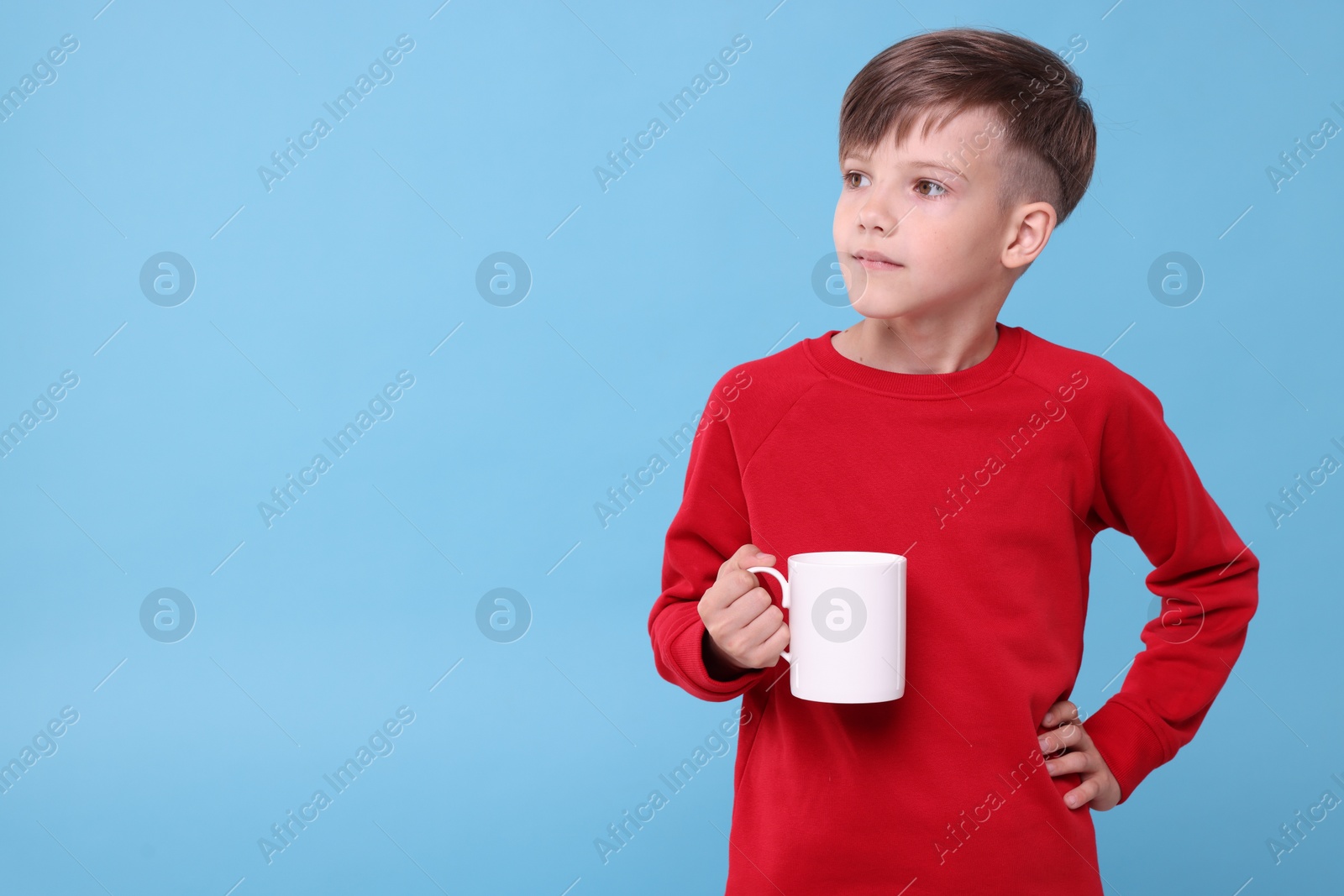 Photo of Cute boy with white ceramic mug on light blue background, space for text