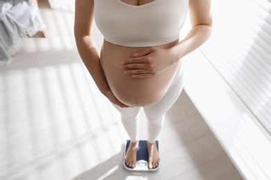 Photo of Pregnant woman standing on scales indoors, closeup