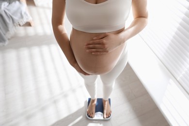 Pregnant woman standing on scales indoors, closeup