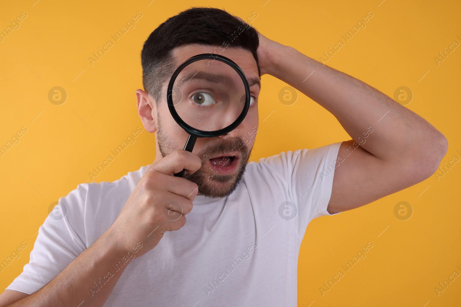 Photo of Surprised man looking through magnifier glass on yellow background