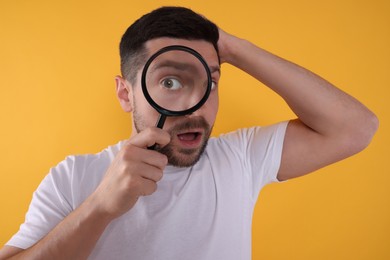Photo of Surprised man looking through magnifier glass on yellow background