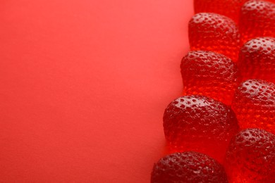 Photo of Delicious gummy strawberry candies on red background, closeup. Space for text