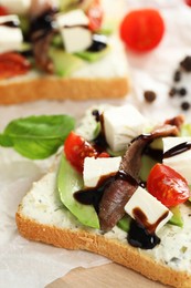 Delicious sandwiches with anchovies, cheese, tomatoes and sauce on wooden table, closeup