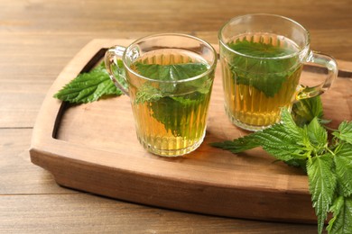 Photo of Glass cups of aromatic nettle tea and green leaves on wooden table