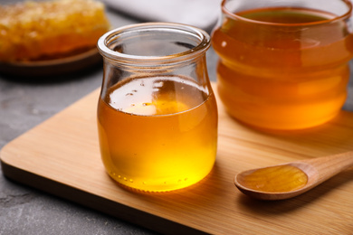 Photo of Tasty aromatic honey and wooden board on grey table