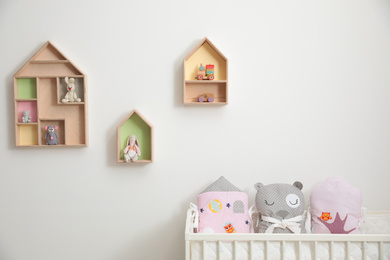Stylish house shaped shelves with toys and crib in nursery. Baby room interior design