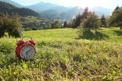 Photo of Red alarm clock on green mountain meadow in morning