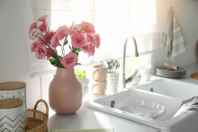 Photo of Vase with flowers on countertop near sink against window in kitchen