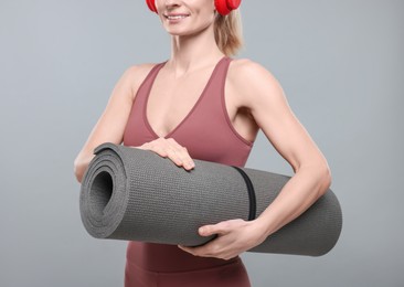 Sportswoman with headphones and fitness mat on grey background, closeup
