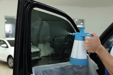 Worker spraying water onto tinted car window  in workshop, closeup