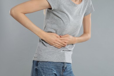 Young woman suffering from liver pain on grey background, closeup