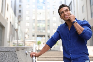 Photo of Handsome young African-American man talking on mobile phone outdoors. Space for text