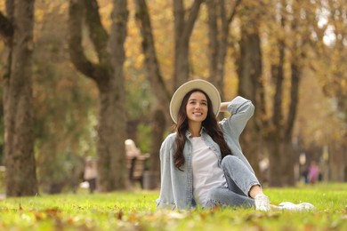 Photo of Young woman sitting on green grass in park, space for text