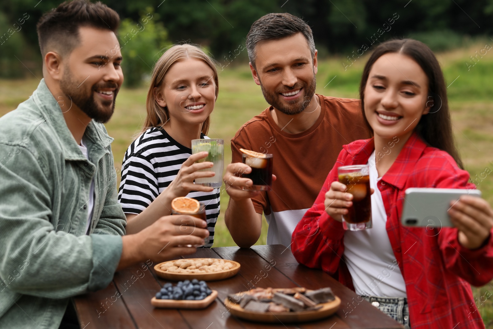 Photo of Happy friends with glasses of cocktails taking selfie at table outdoors