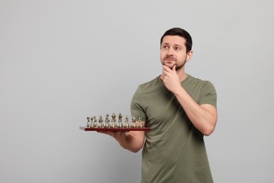 Photo of Thoughtful man holding chessboard with game pieces on light grey background. Space for text