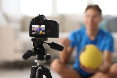 Smiling sports blogger holding ball while recording fitness lesson at home, focus on camera. Space for text
