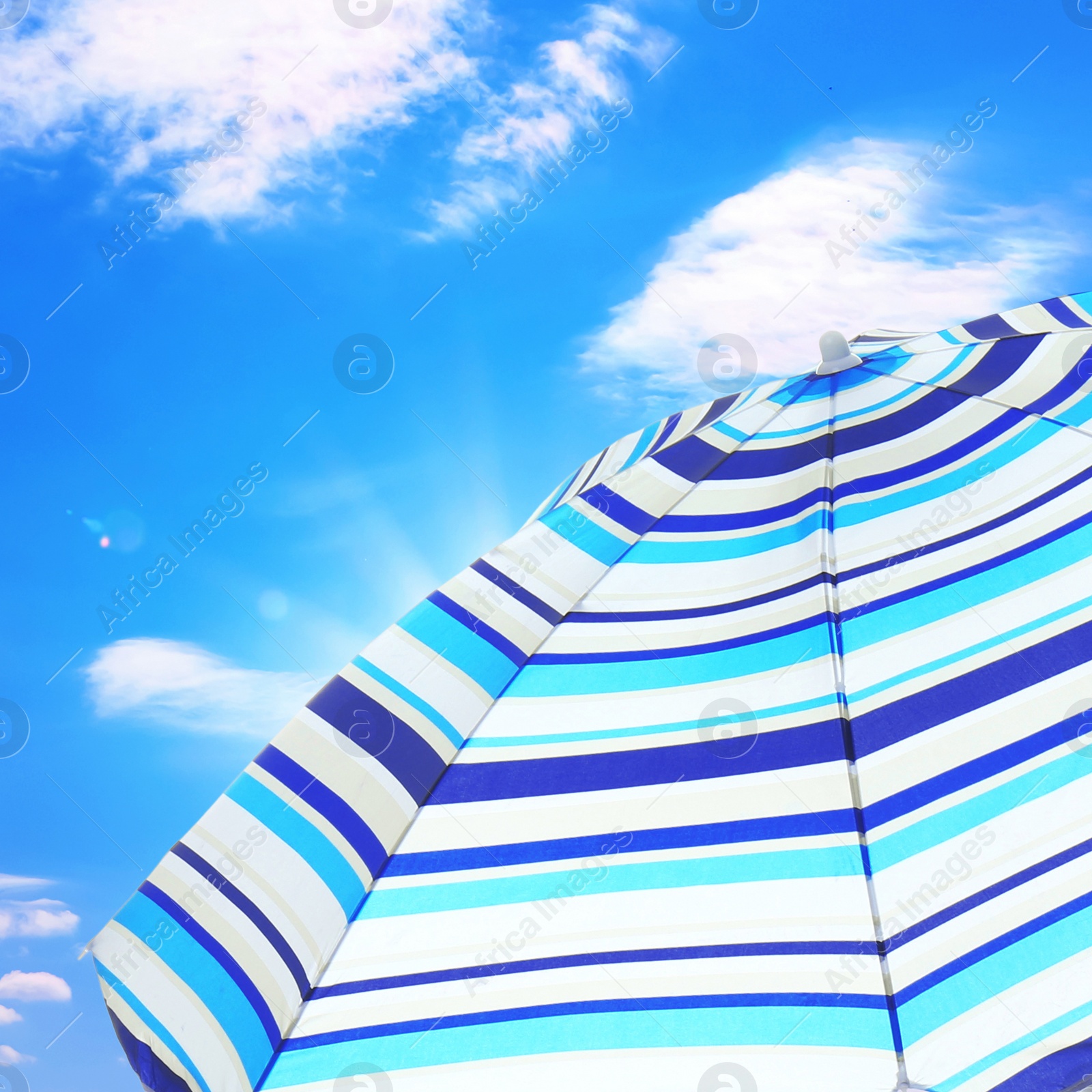 Image of Open big striped beach umbrella and beautiful blue sky with white clouds on background