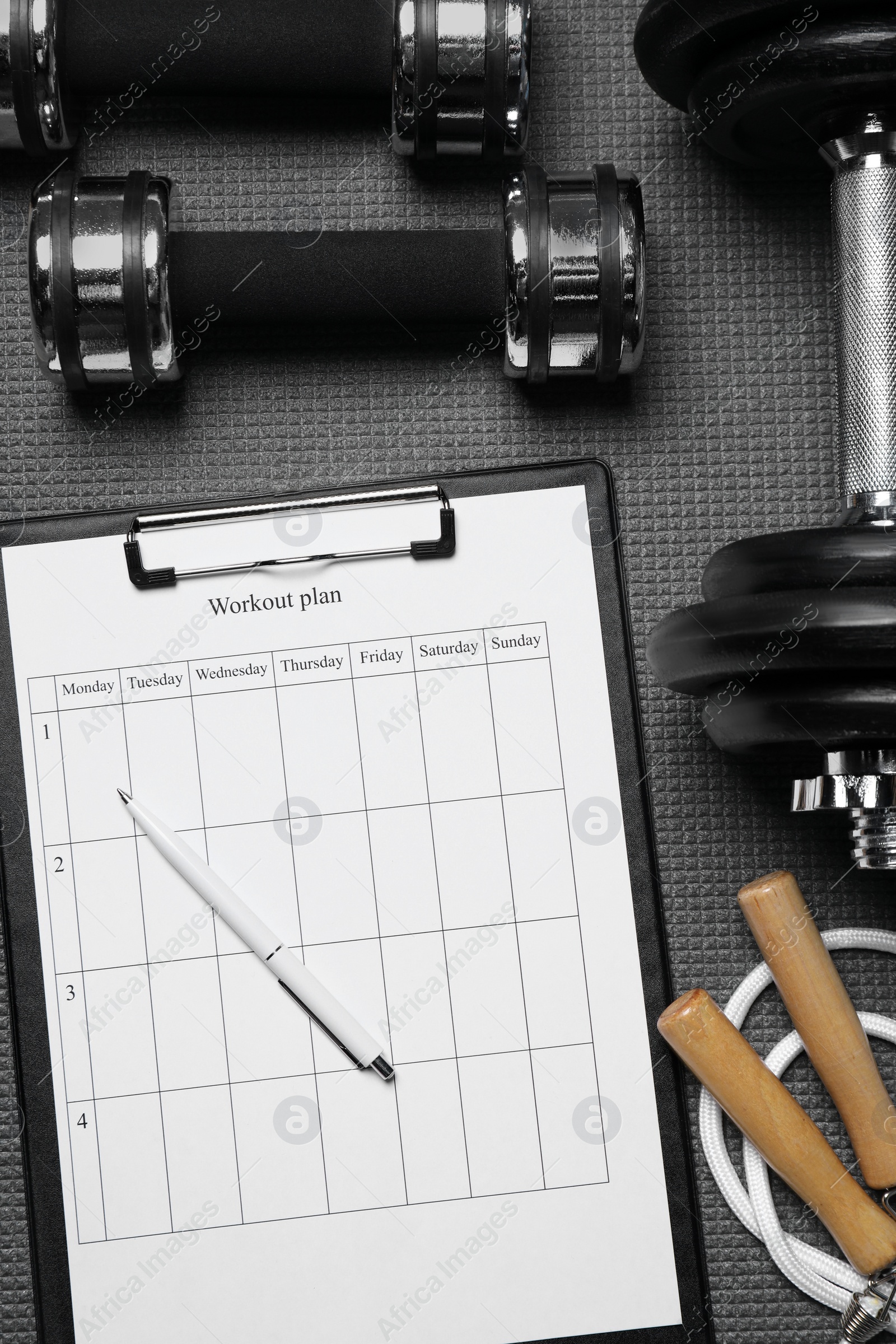 Photo of Clipboard with workout plan and sports equipment on black mat, flat lay. Personal training