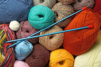 Photo of Different balls of woolen knitting yarns and needles as background, top view