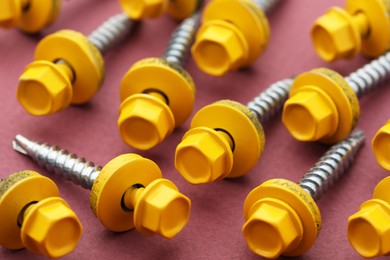 Yellow self-tapping screws on pink background, closeup