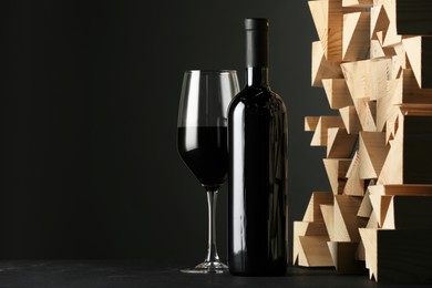 Stylish presentation of red wine in bottle and wineglass on black background, space for text