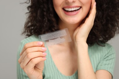 Photo of Young woman holding teeth whitening strips on grey background, closeup. Space for text