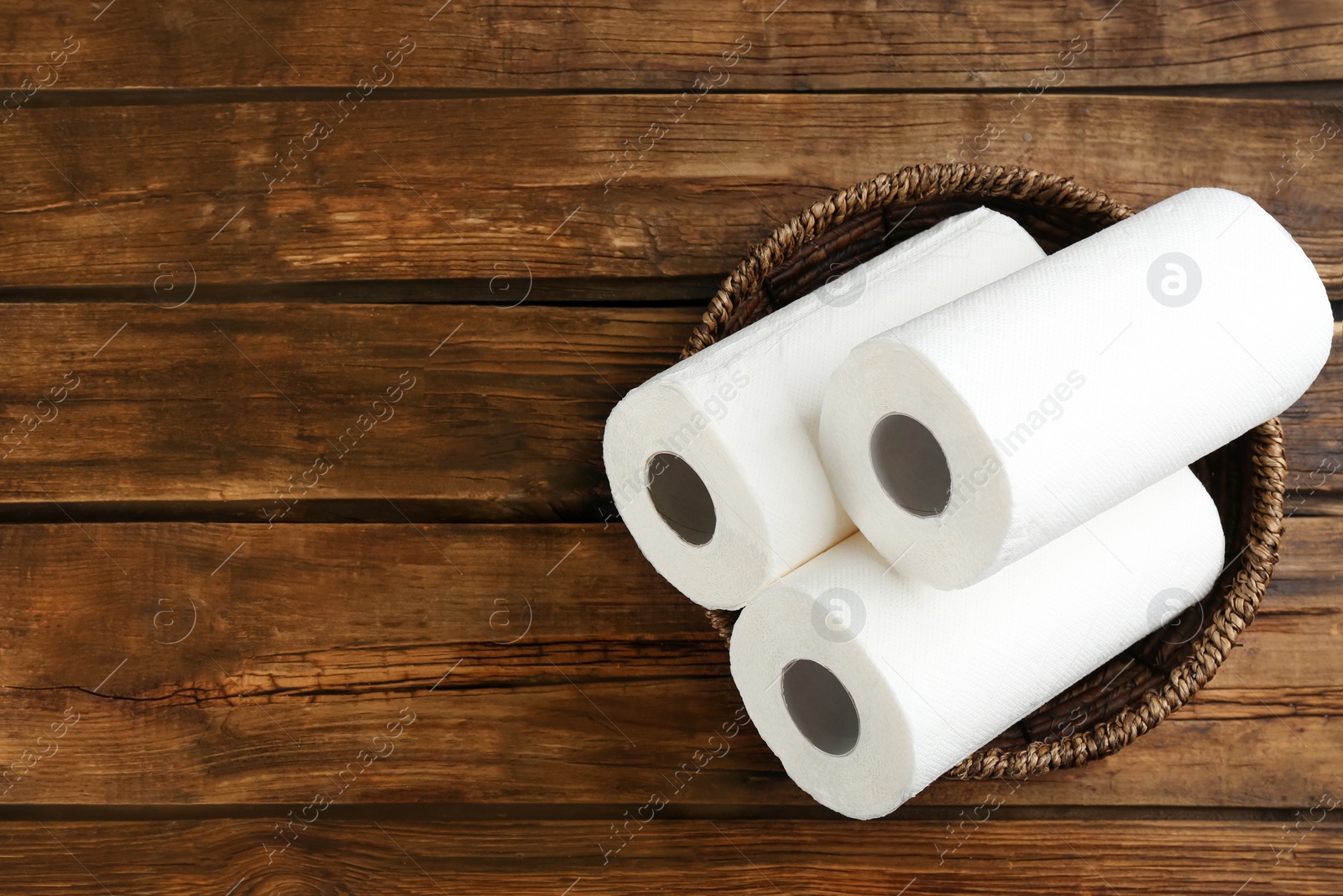 Photo of Rolls of paper towels in wicker basket on wooden table, top view. Space for text