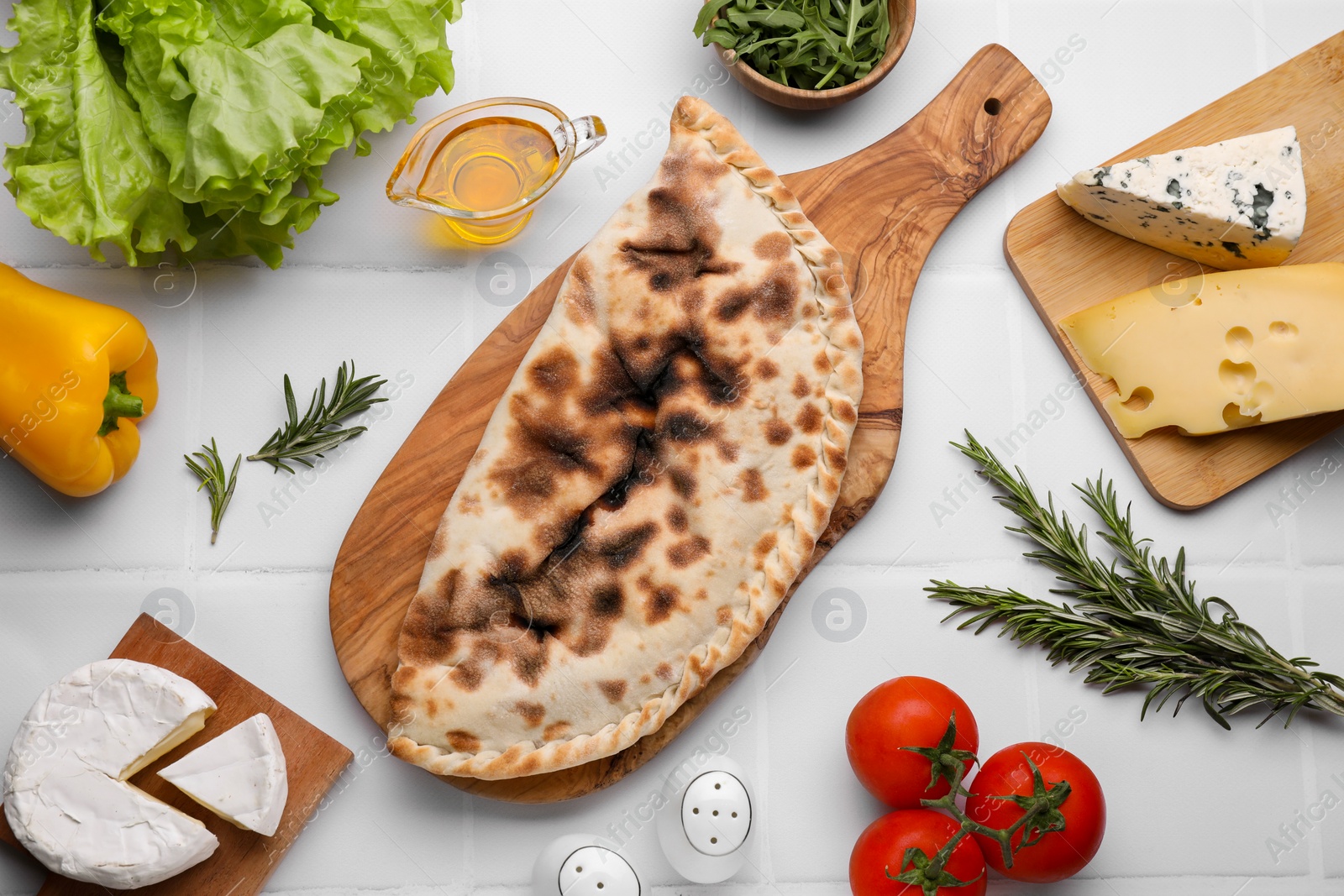 Photo of Tasty pizza calzone with cheese and different products on white tiled table, flat lay