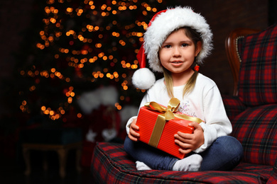 Cute little child with Christmas gift sitting in armchair at home