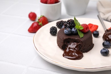 Photo of Plate with delicious chocolate fondant, berries and mint on white table, closeup. Space for text