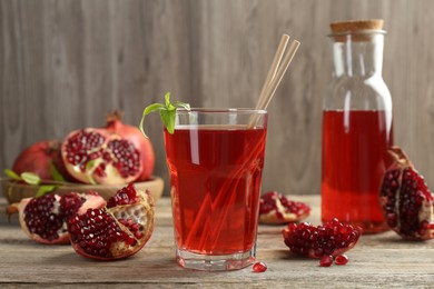 Photo of Tasty pomegranate juice in glass and fresh fruits on wooden table