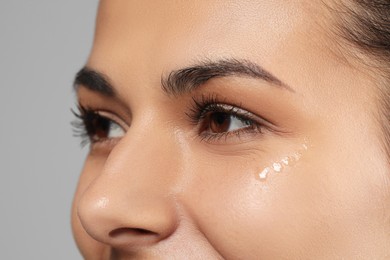 Photo of Woman with eye cream on grey background, closeup. Skin care