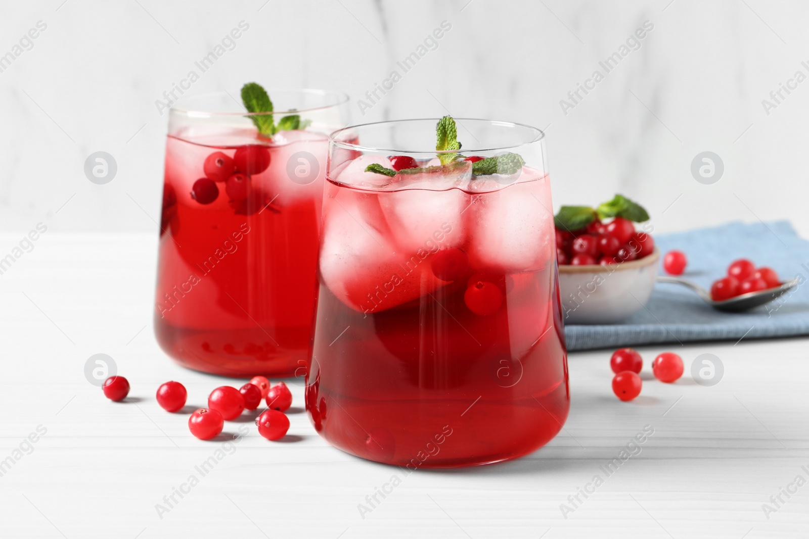 Photo of Tasty cranberry juice with ice cubes in glasses and fresh berries on white wooden table, closeup