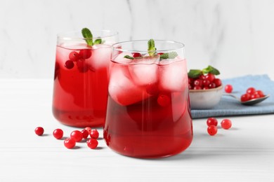 Tasty cranberry juice with ice cubes in glasses and fresh berries on white wooden table, closeup
