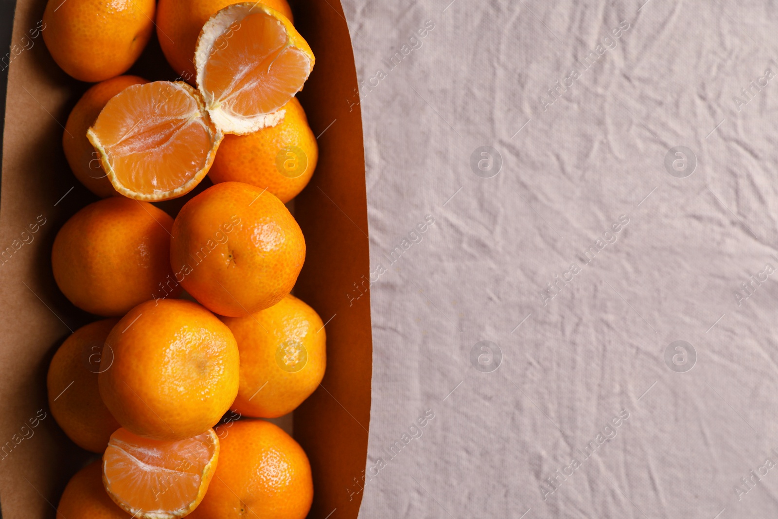 Photo of Paper box with fresh ripe tangerines on beige cloth, top view. Space for text