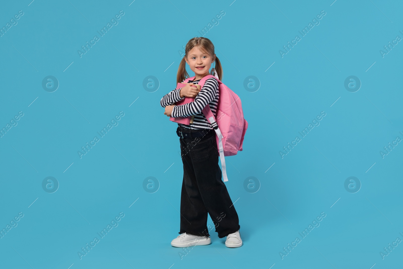 Photo of Happy schoolgirl with backpack and books on light blue background