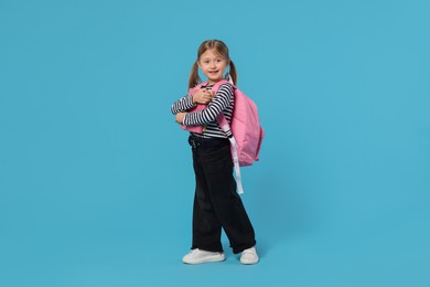 Photo of Happy schoolgirl with backpack and books on light blue background