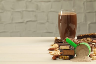 Different energy bars, nuts, protein cocktail and powder on white wooden table. Space for text