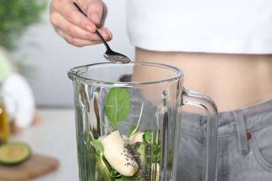 Woman adding chia seeds into blender with ingredients for green smoothie indoors, closeup