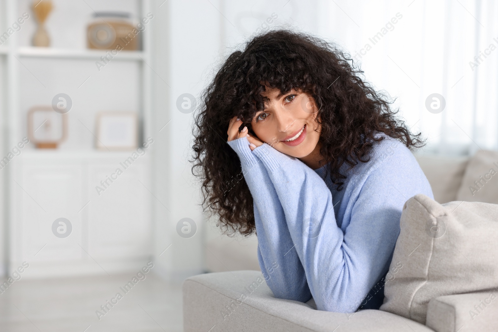 Photo of Happy young woman in stylish light blue sweater indoors, space for text