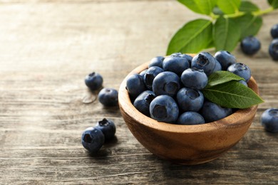 Photo of Bowl of fresh tasty blueberries on wooden table, space for text